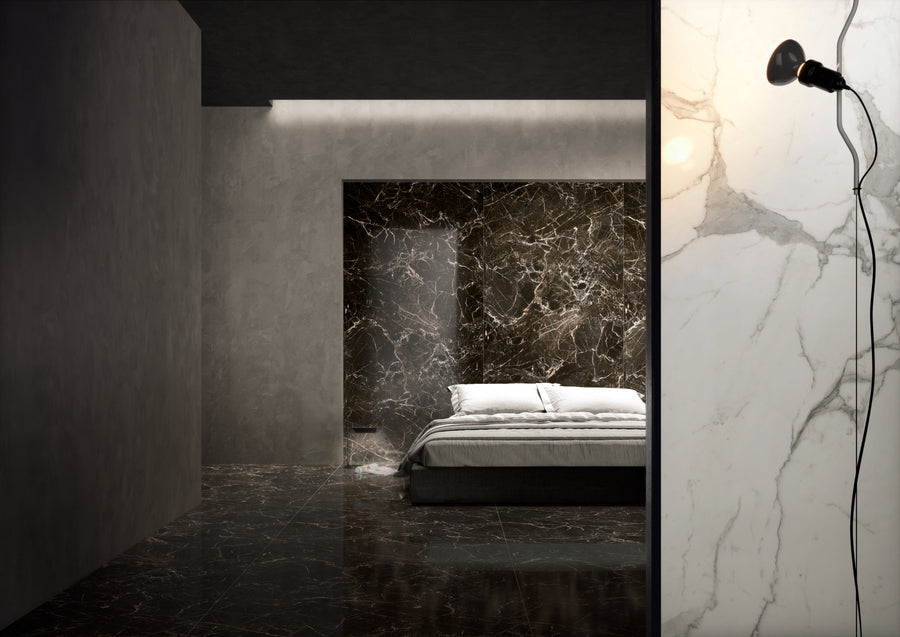 A minimalist bedroom features a bed with white bedding against a dark marble wall and floor. The adjoining room has a white marble wall with a black lamp attached. The space is modern and dimly lit.