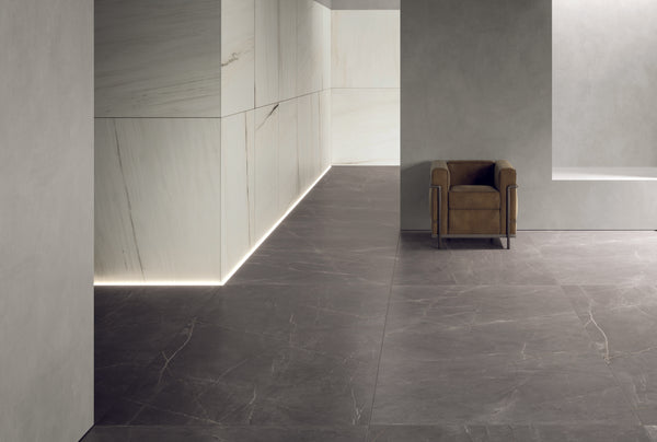 A modern minimalist interior with large gray marble tiles, light stone-paneled walls, and an accent chair upholstered in brown leather. Soft LED lighting highlights the wall edges.