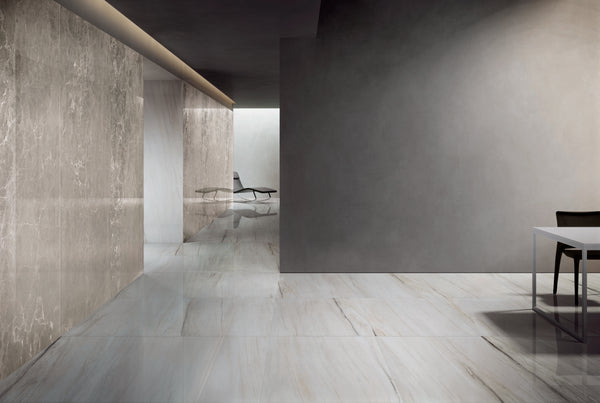 A modern, minimalistic interior with polished marble floors and walls, a gray table with a black chair on the right, and a lounge chair visible in a bright area at the back.
