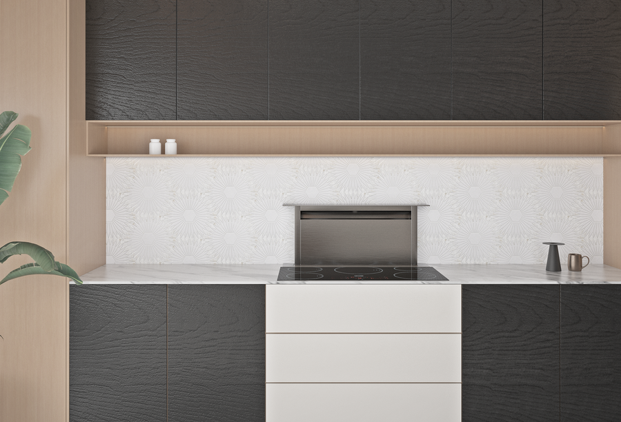 Modern kitchen with black textured cabinets, white drawers, a marble countertop, a black electric cooktop, a white floral backsplash, two small jars on a shelf, a black kettle, and a green plant on the left.