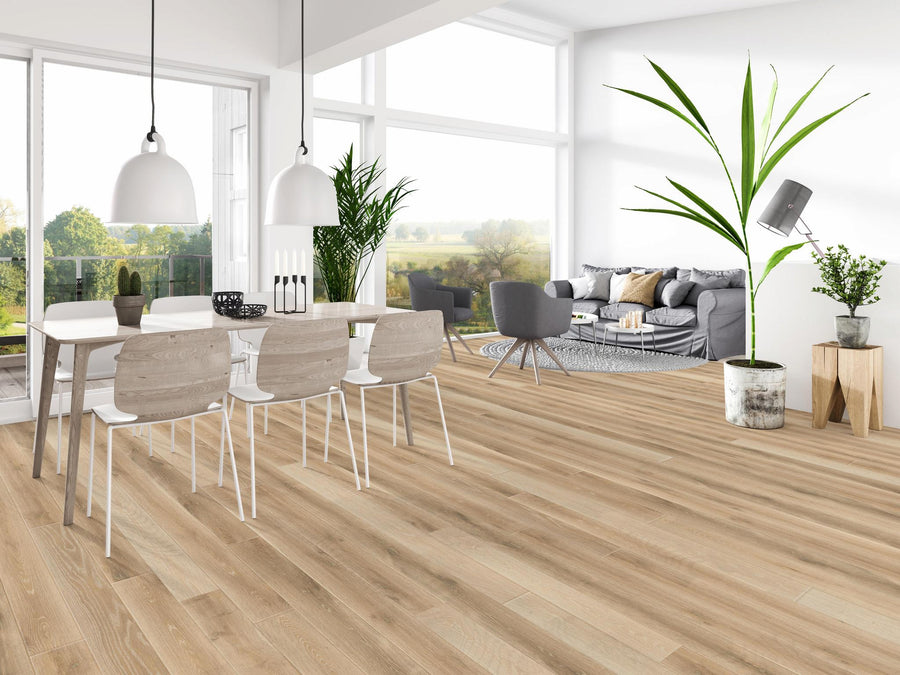 Modern open-concept living and dining area with large windows, light wood flooring, white dining table and chairs, grey sofa, indoor plants, pendant lights, and a view of greenery outside.