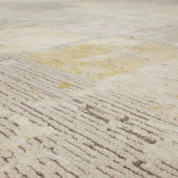 Close-up view of a modern area rug featuring a textured pattern with beige, cream, gray, and subtle gold tones, creating a soft and abstract geometric design.