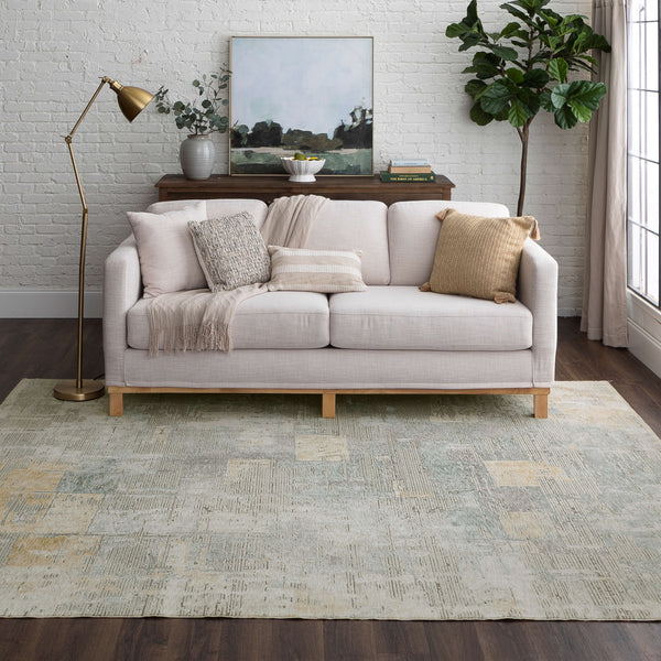 A modern living room with a light-colored sofa, neutral pillows, and a throw blanket. Behind the sofa is a console table with decor and art. A floor lamp, potted plant, and large window complete the cozy, stylish space.