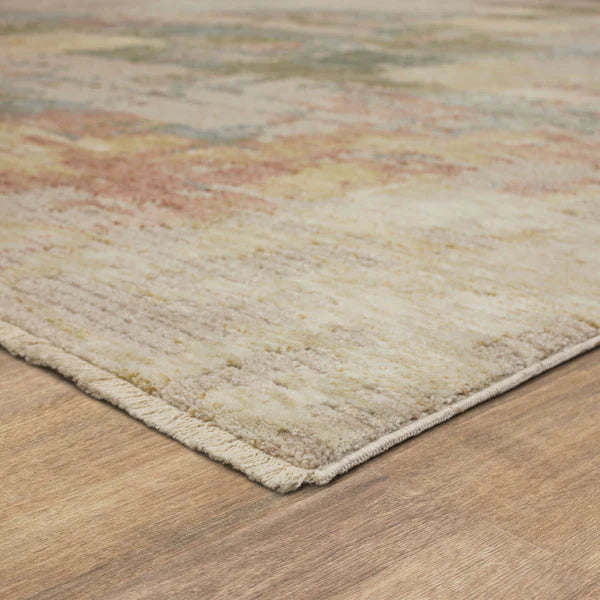 A close-up of a rectangular area rug with a muted, multicolored pattern, featuring soft shades of beige, yellow, pink, and blue, placed on a light wooden floor.