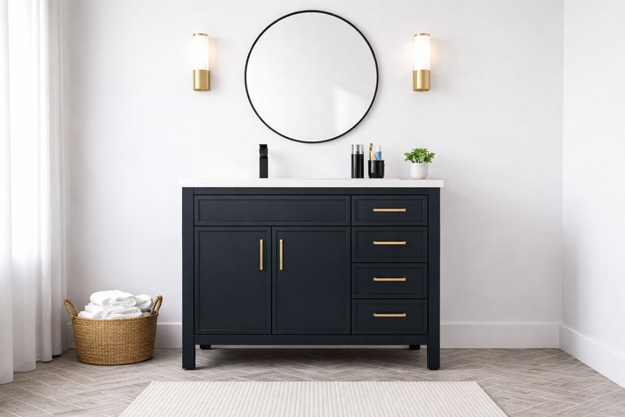 The Novello 36" Vanity features a modern black cabinet with gold handles, a white countertop, a round mirror above, two gold wall sconces on either side, and a basket of white towels placed on the floor next to it.