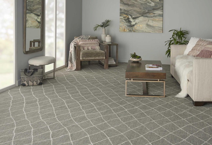A modern living room with a light gray patterned carpet, white sofa, wooden coffee table, armchair, throw blanket, decorative items, large wall art, and mirrored closet doors.