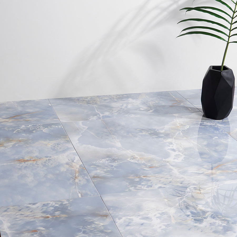 Large, glossy tiles with a blue and white marbled pattern cover the floor. A black geometric vase holding a green plant sits in the corner, and soft shadows are cast on a plain white wall.