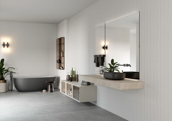 Modern bathroom with a freestanding black bathtub, minimalist sink with a large mirror, wall-mounted shelves, indoor plants, and soft lighting fixtures on white tiled walls and gray flooring.