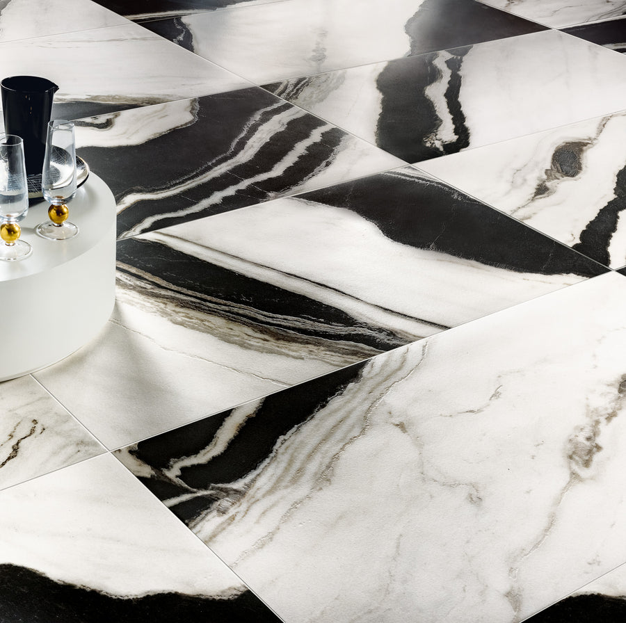 Large, glossy black and white marble tiles with bold, swirling patterns are arranged diagonally. In the corner, a white round table holds a black ice bucket and glasses with a golden liquid.