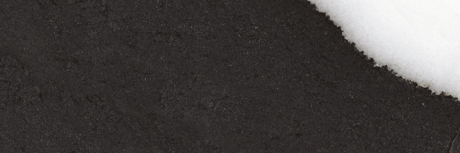 A close-up view of a surface with a black, rough-textured area on the left and a smooth, white, snow-like layer on the upper right, creating a diagonal boundary between the two.