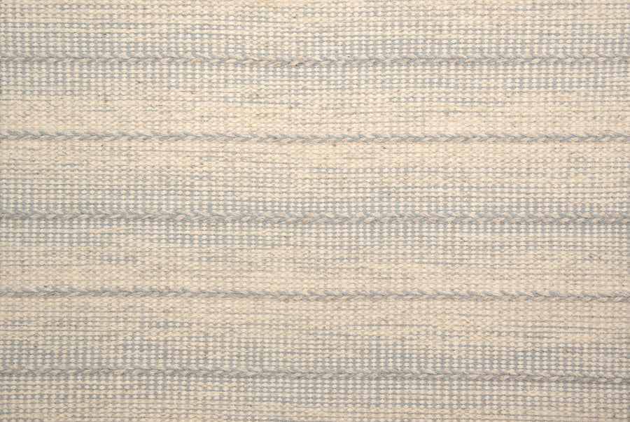 A close-up of Orzola On Trend Carpet reveals textured, woven fabric in soft beige and gray—horizontal lines create a subtle striped, grid-like pattern, ideal for modern interiors and contemporary design.