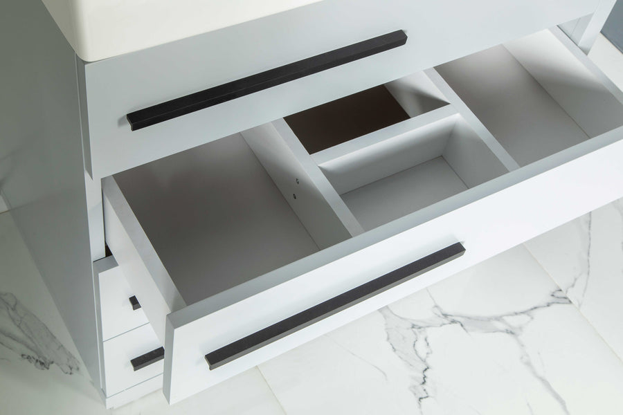 A top-down view of an open bathroom vanity drawer with multiple compartments, featuring modern black handles and placed on a white marble tile floor with gray veining.