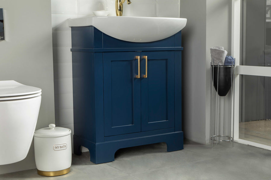 A modern bathroom features a blue vanity with gold handles, a white sink, a white toilet, a round white container labeled MY BATH, and a metal stand holding towels in the corner.