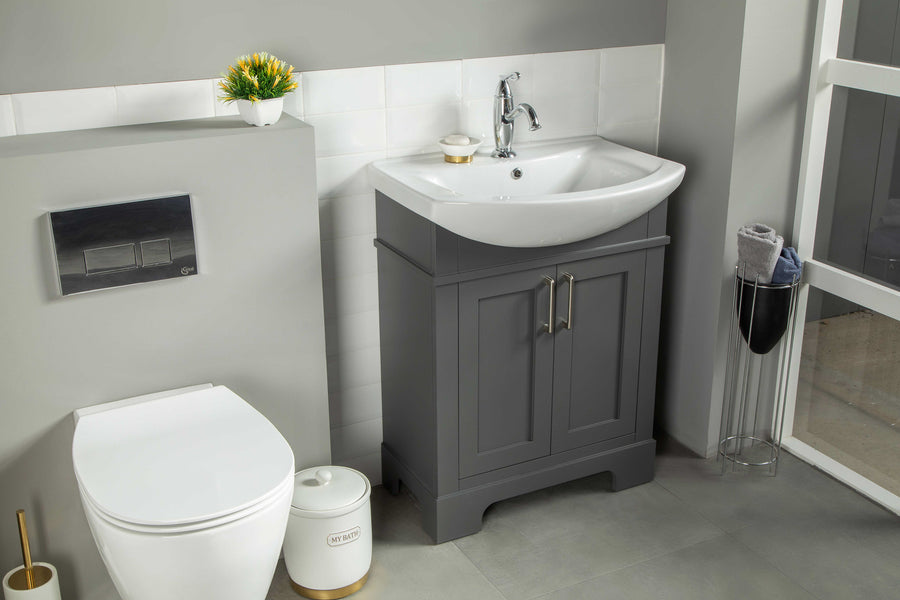 Modern bathroom with a white toilet, a gray vanity with sink and silver faucet, white tile backsplash, a small plant, and a towel stand by a window. The space is clean, tidy, and well-lit.