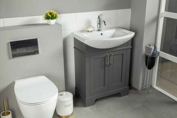 Modern bathroom with a white toilet, a gray vanity with sink and silver faucet, white tile backsplash, a small plant, and a towel stand by a window. The space is clean, tidy, and well-lit.