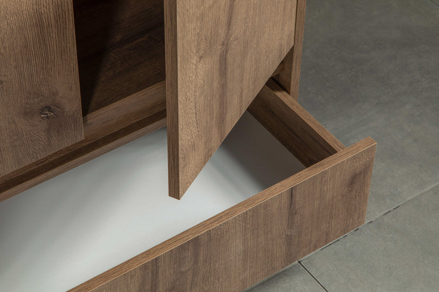 A close-up of a wooden cabinet with one door slightly open and a lower drawer pulled out, revealing an empty white interior. The cabinet stands on a gray tiled floor.