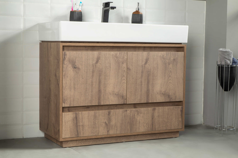 A modern bathroom vanity with a wood finish, white rectangular sink, black faucet, toothbrushes, soap dispenser, and a towel on a rack nearby, set against white tiled walls and a gray floor.