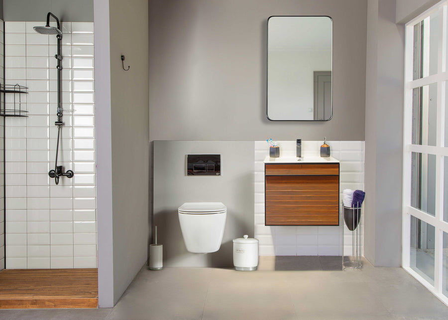 Modern bathroom with a walk-in shower, wall-mounted toilet, floating wooden vanity with sink, mirror, trash bin, and glass container holding rolled towels; neutral tones and ample natural light.