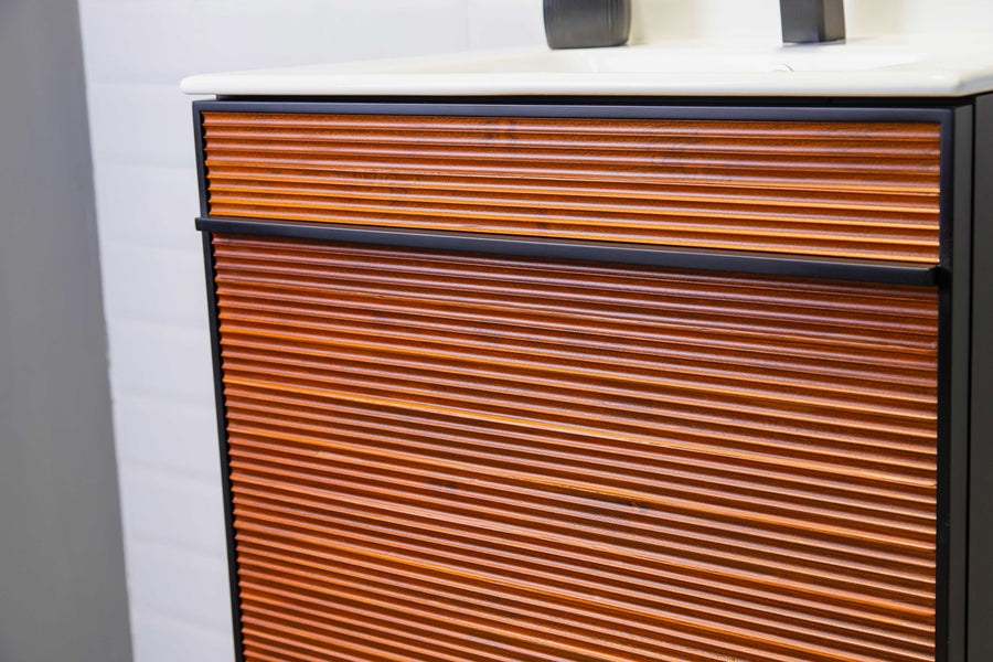 A close-up of a modern bathroom vanity with horizontal wooden slats and black trim, topped with a white countertop and a faucet.