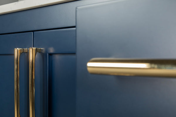 Close-up of blue kitchen cabinets with sleek gold handles, featuring a marble countertop above. The focus is on the modern design and contrasting colors and materials.