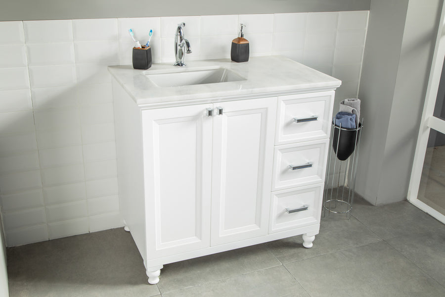 White bathroom vanity with a marble countertop, built-in sink, chrome faucet, two white cabinet doors, and three drawers. Two toothbrush holders and a soap dispenser sit on the counter. Tiled wall and gray floor.