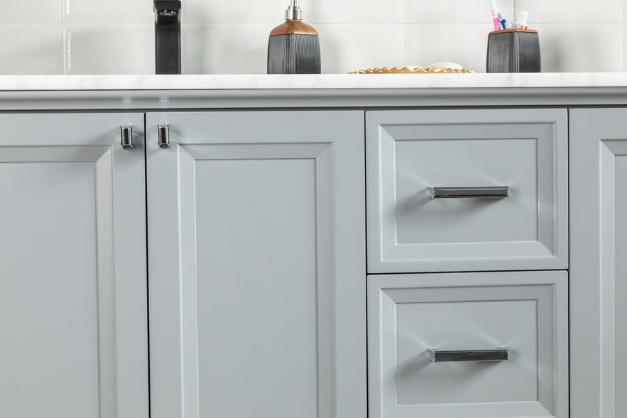 Close-up of light gray bathroom cabinets and drawers with silver handles, beneath a white countertop. On the counter are soap dispensers and a container holding toothbrushes.