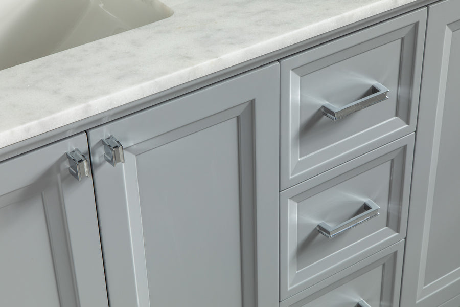 Close-up of a light gray bathroom vanity with a marble countertop, featuring two cabinet doors with chrome handles on the left and three drawers with matching handles on the right. Part of a white sink is visible at the top left.