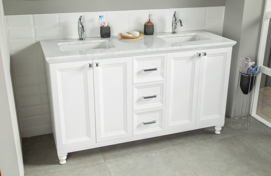 A modern bathroom vanity with a white marble countertop, two sinks, two faucets, and white cabinets. Toothbrushes, soap, and pump bottles are placed on the countertop. The floor is tiled in gray.
