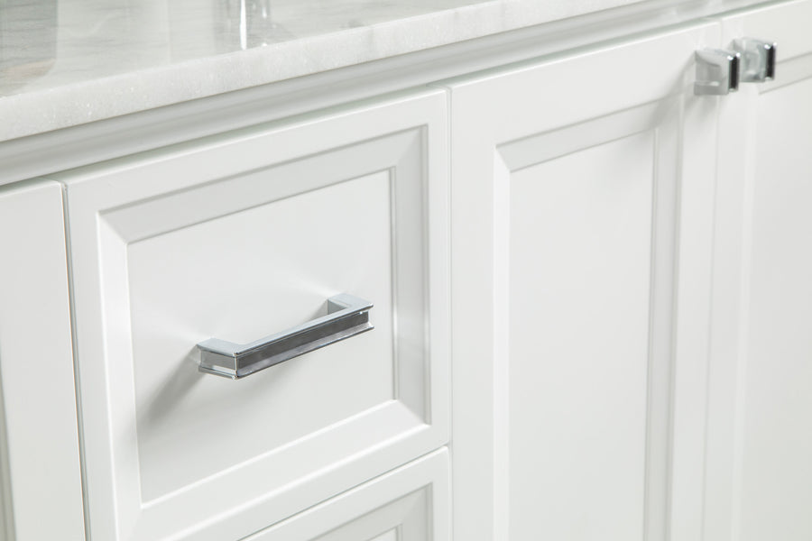 Close-up of white cabinet doors and drawer with silver handles and a white countertop above. The surfaces are clean and the hardware has a modern, sleek design.