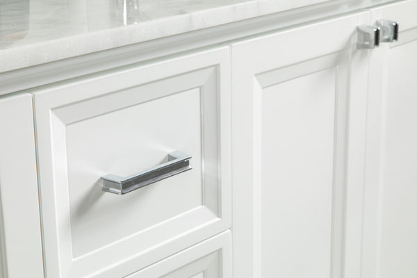 Close-up of white cabinet doors and drawer with silver handles and a white countertop above. The surfaces are clean and the hardware has a modern, sleek design.