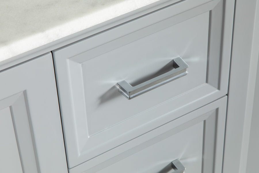Close-up of a gray cabinet drawer with a rectangular silver handle, set beneath a white marble countertop. The drawer features recessed panel detailing.