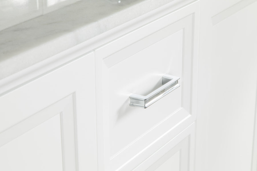 A close-up of a white cabinet with a rectangular silver handle beneath a light-colored marble countertop. The cabinet has a clean, modern design with paneled detailing.