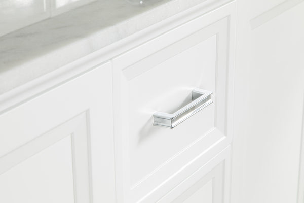 A close-up of a white cabinet with a rectangular silver handle beneath a light-colored marble countertop. The cabinet has a clean, modern design with paneled detailing.