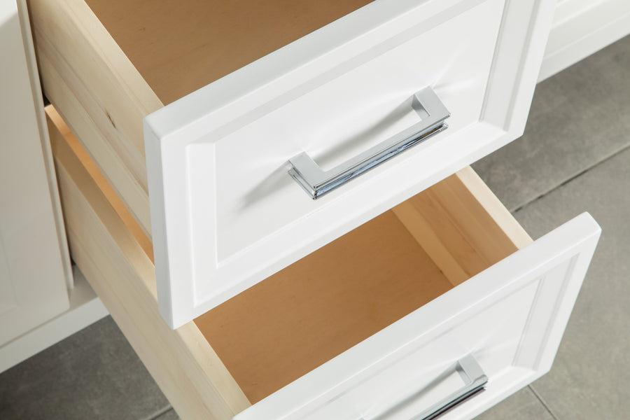 Two white cabinet drawers with silver handles are partially open, revealing empty light wood interiors. The drawers are set against a tiled floor.