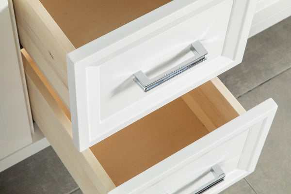 Two white cabinet drawers with silver handles are partially open, revealing empty light wood interiors. The drawers are set against a tiled floor.