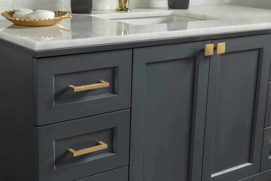 Close-up of a modern bathroom vanity with matte dark blue cabinets, gold handles, and a white countertop. A decorative gold tray with soaps sits near a rectangular sink under a brass faucet.