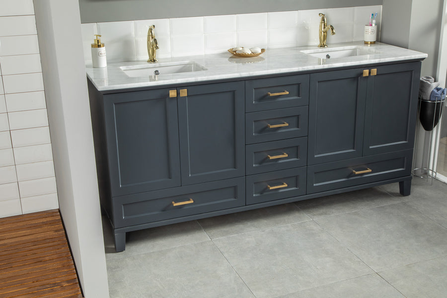 Modern double-sink bathroom vanity with dark blue cabinets, gold handles, and a white marble countertop. Two faucets, a soap dispenser, and a dish with small items are visible. Gray tile floor and white tiled wall.