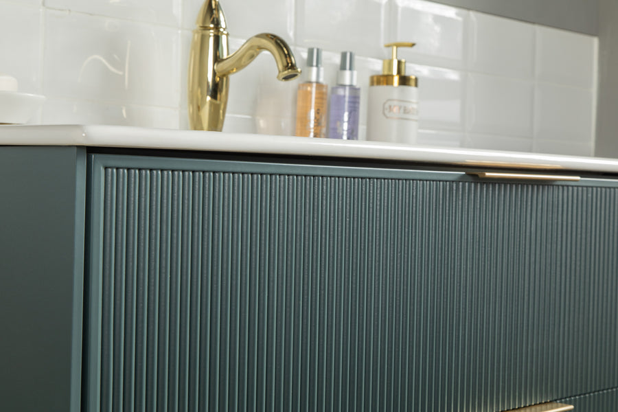 Close-up of a modern bathroom vanity with a green ribbed cabinet, gold faucet, white countertop, and toiletries, set against a white subway tile backsplash.