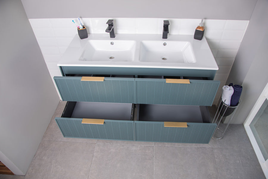 A modern bathroom vanity with two sinks, two toothbrush holders, soap dispensers, and four blue drawers with gold handles, shown open. Rolled towels are on a small stand nearby.