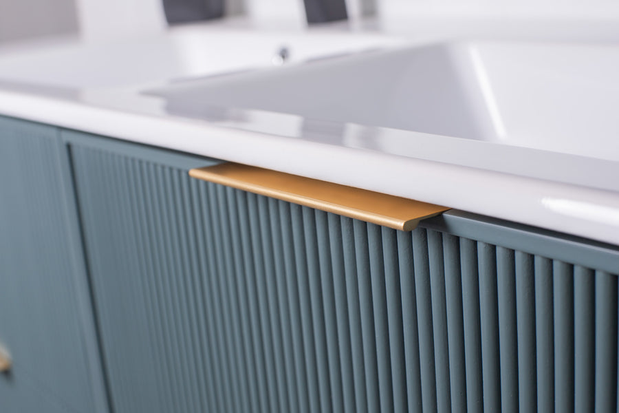 Close-up of a modern bathroom vanity with vertical textured blue-green cabinet doors and a sleek gold handle beneath a white countertop.