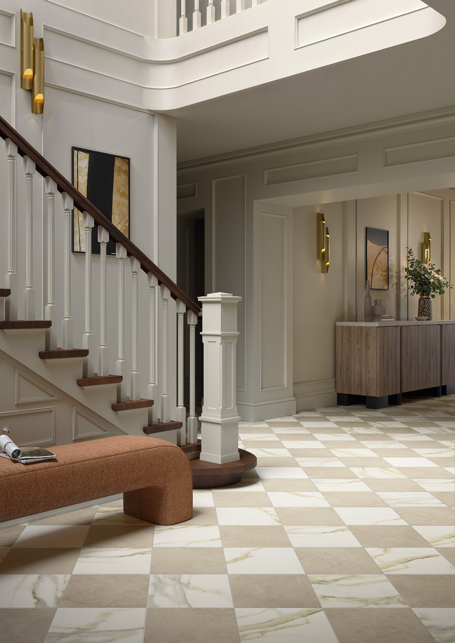 A modern foyer with a floor of Royal Marbles Marfil Select 12x12 Glazed Porcelain Tile, a wooden staircase with white balusters, a rust bench, abstract art, and a wooden console table with flowers—ideal for sophisticated interiors.