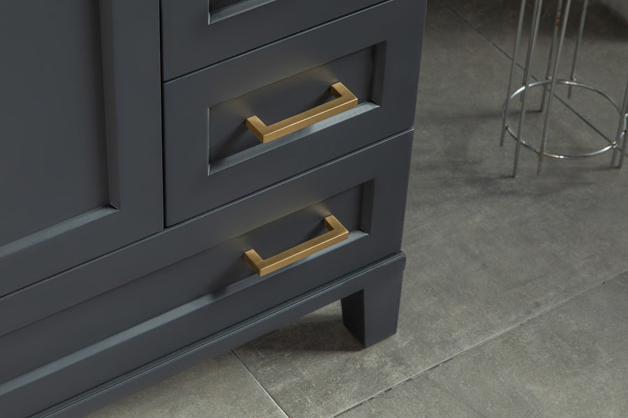 A close-up of a dark gray cabinet with two drawers, each featuring a rectangular gold handle. The cabinet sits on a tiled floor, and part of a metal stool is visible in the background.