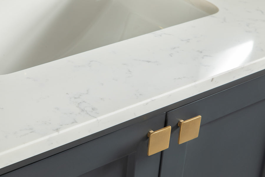 Close-up of a white marble bathroom countertop with subtle gray veining, featuring a sink basin and dark gray cabinet doors with square gold handles underneath.