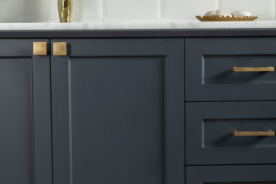 A close-up of dark blue kitchen cabinets and drawers with gold handles, topped with a white countertop. On the counter, there is a gold tray with white objects and a gold vase. White tiled wall in the background.