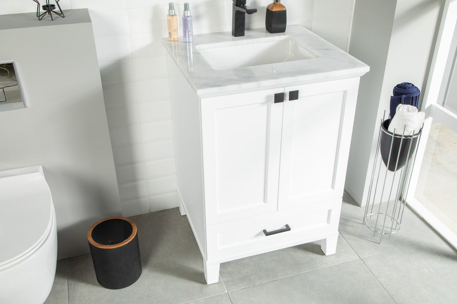 A modern bathroom with a white vanity sink, marble countertop, soap dispensers, a black trash bin, and a tall metal towel holder with rolled towels on a gray tiled floor.