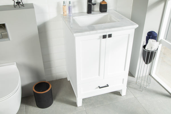 A modern bathroom with a white vanity sink, marble countertop, soap dispensers, a black trash bin, and a tall metal towel holder with rolled towels on a gray tiled floor.