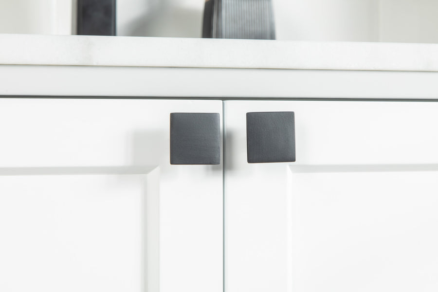 Close-up of two white cabinet doors with modern, square-shaped black handles beneath a white countertop. The design is minimalistic and contemporary.