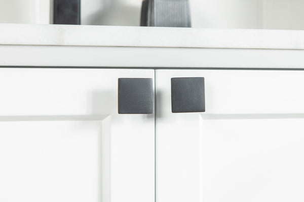 Close-up of two white cabinet doors with modern, square-shaped black handles beneath a white countertop. The design is minimalistic and contemporary.