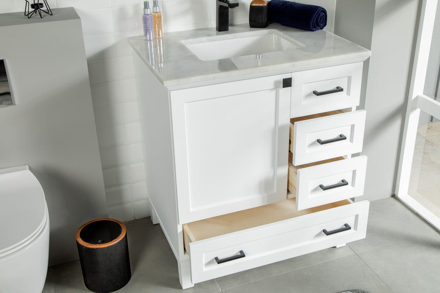 A white bathroom vanity with a marble countertop, a sink, and a single cabinet door. Three drawers on the right side are open, showing empty interiors. Toiletries and a rolled towel are on the counter.