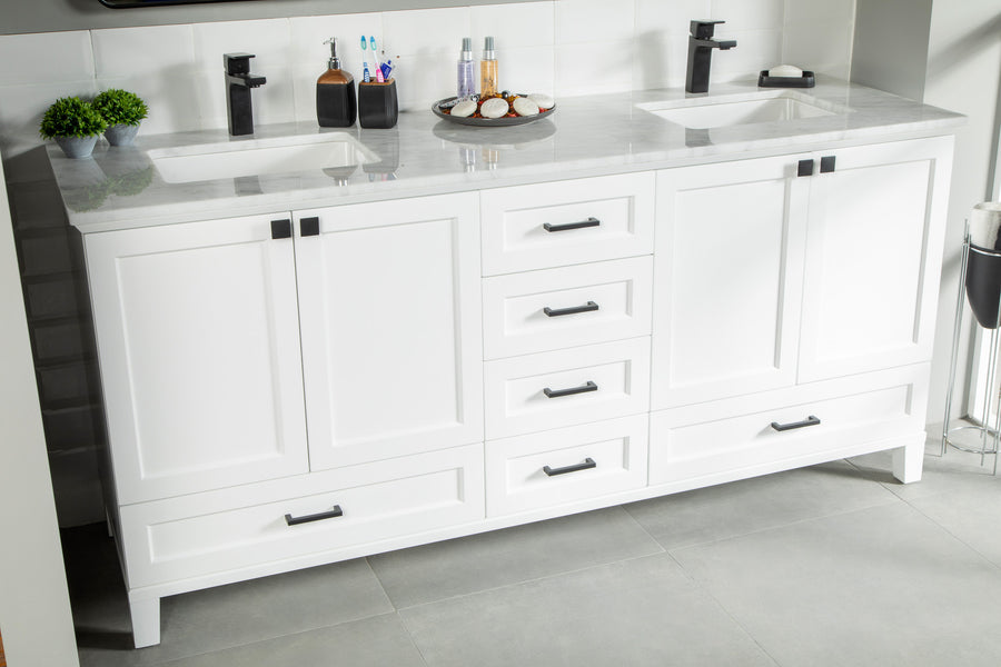 White double-sink bathroom vanity with a marble countertop, black fixtures, six drawers, and two cabinets. Toiletries, soap dispensers, and a small plant are arranged on the counter. The floor is gray tile.
